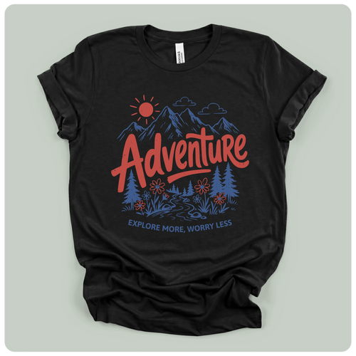 A black short-sleeve graphic t-shirt laid flat on a light gray background. The shirt features a colorful graphic print with a red 'Adventure' text, blue mountains, trees, and a sun, with the phrase 'EXPLORE MORE, WORRY LESS' printed below.