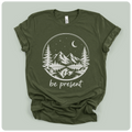 short-sleeve t-shirt with a white graphic print of a mountain landscape at night with the text 'be present' underneath, laid flat on a light sage green background.