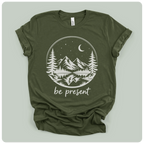 short-sleeve t-shirt with a white graphic print of a mountain landscape at night with the text 'be present' underneath, laid flat on a light sage green background.