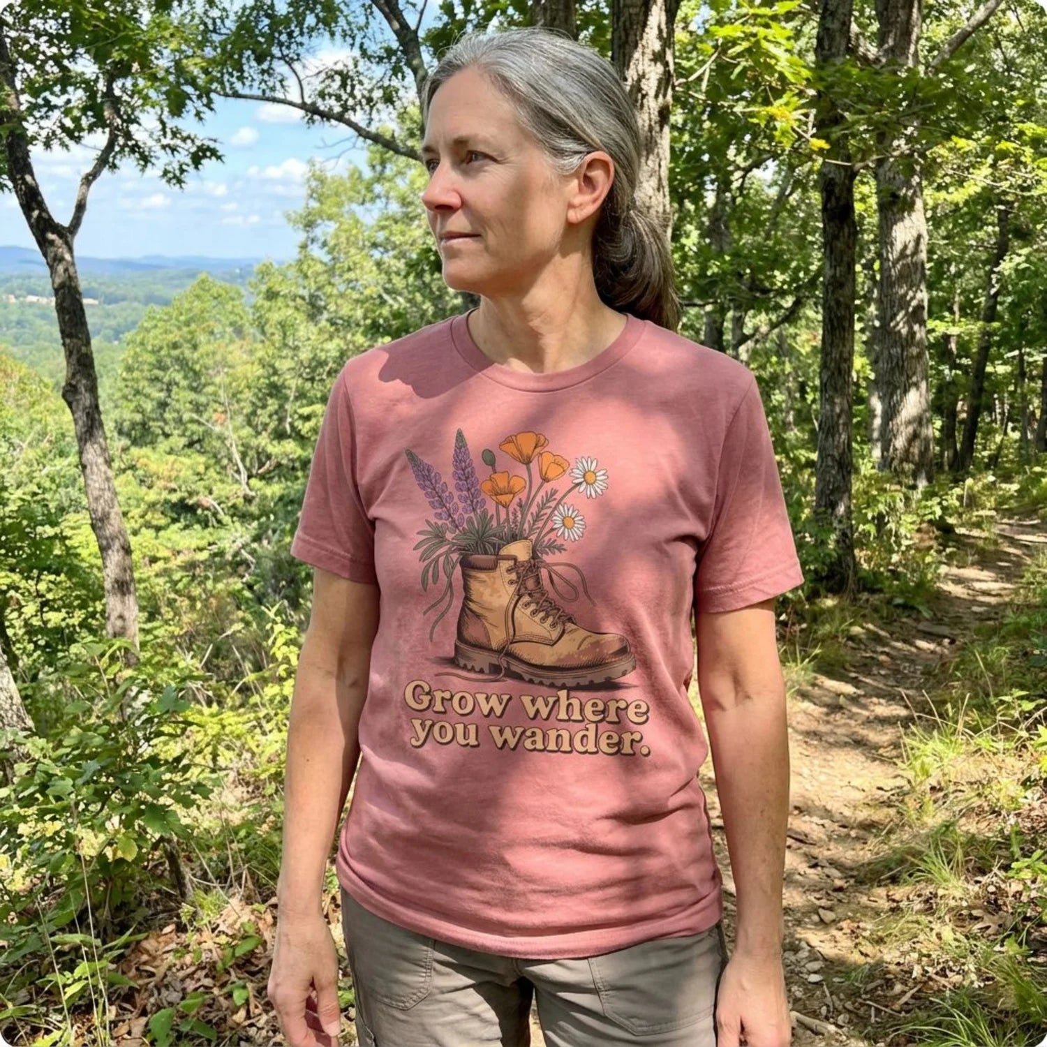 Dusty rose hiking t-shirt with boot and wildflowers graphic on forest trail