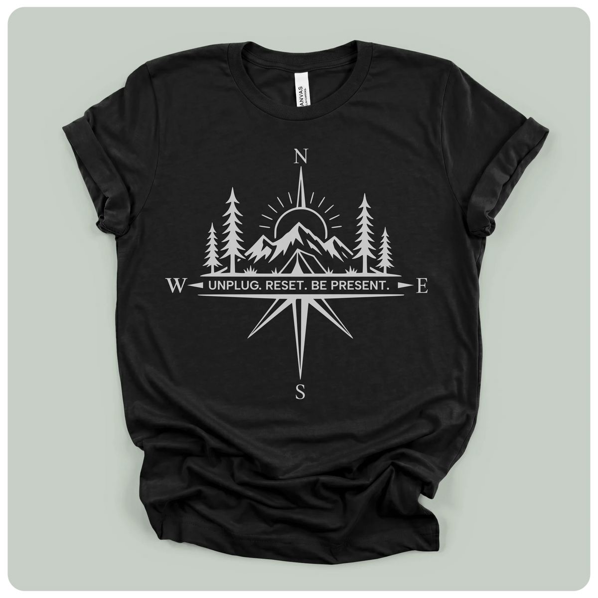 A black short-sleeve crewneck t-shirt with a white graphic print of a compass rose, mountains, pine trees, and a sun, with the text 'W UNPLUG. RESET.